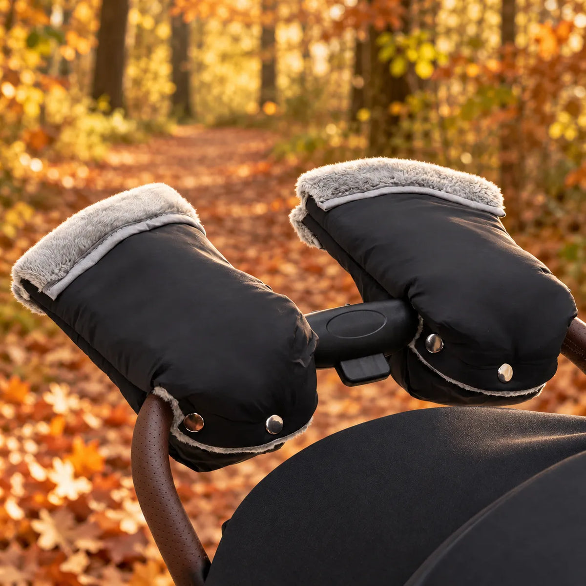 Black " DERYAN " hand warmers with gray fleece lining attached to a stroller in an autumn forest